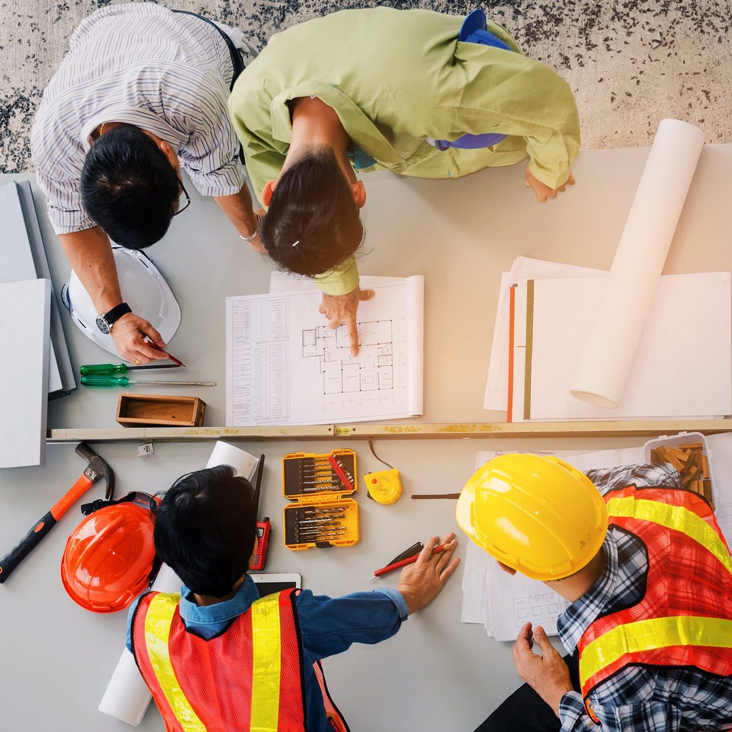 top view of group of engineer, technician and architect planning about building plan with blueprint and construction tools on the conference table at construction site, business and industry concept