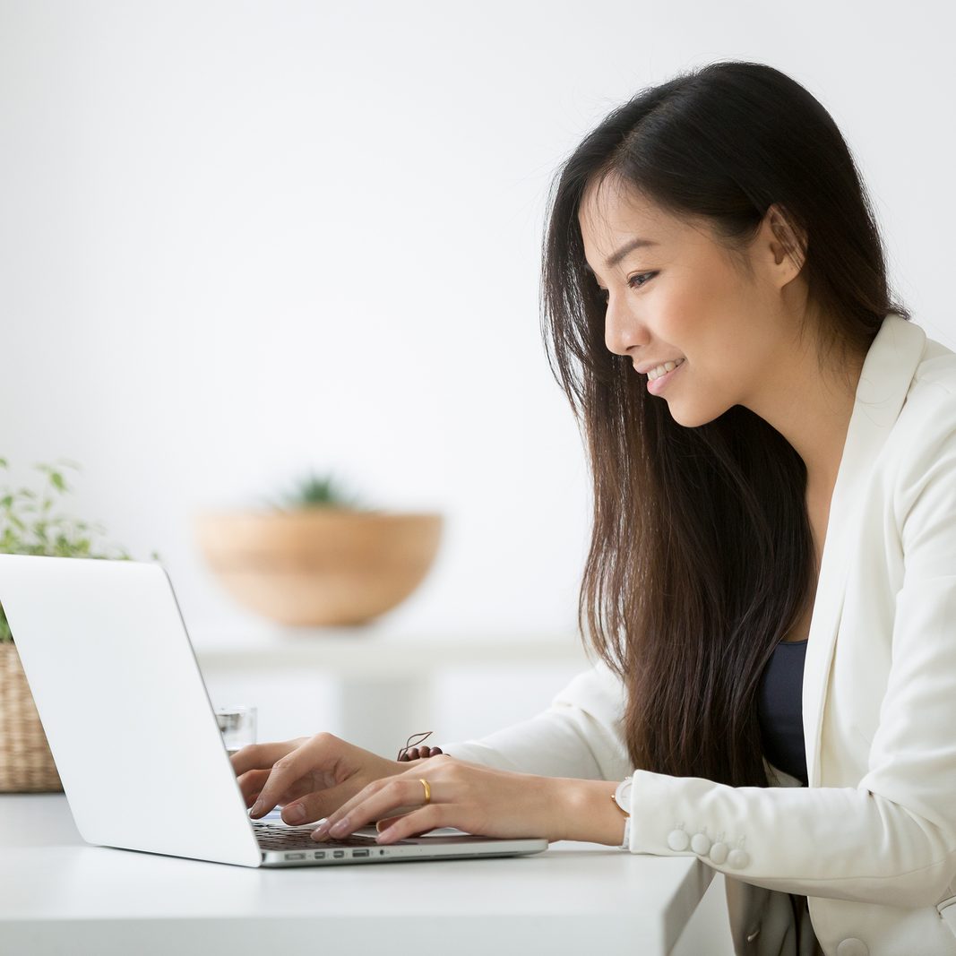 Smiling young asian businesswoman using computer at home office workplace, happy korean employee working on laptop, attractive japanese or chinese woman student studying communicating online with pc